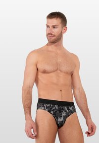Schwarze bedruckte Unterhosen aus weichem Stoff mit einem strukturierten Blumenmuster und einem schwarzen elastischen Bund, auf dem der Markenname zu sehen ist.