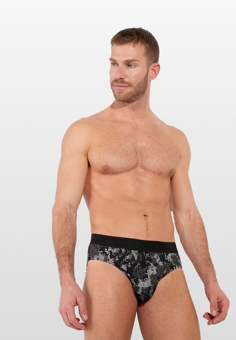 Schwarze bedruckte Unterhosen aus weichem Stoff mit einem strukturierten Blumenmuster und einem schwarzen elastischen Bund, auf dem der Markenname zu sehen ist.