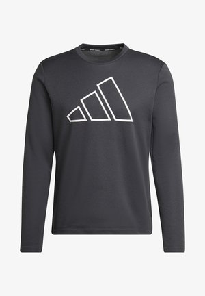 Homme portant un t-shirt à manches longues foncé avec un grand logo Adidas et un pantalon Adidas noir avec des bandes blanches.