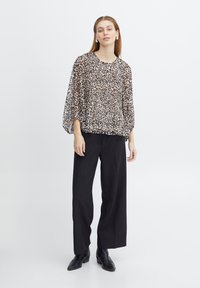 Tigrinis raštas permatomas marškinėlių blouse su plačiomis rankovėmis, derinamas su juodomis kelnėmis aukštu liemeniu. Modelis vilki juodais auliniais batais ir sidabrinėmis auskarėliais.