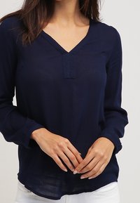Marineblaues Langarmbluse mit V-Ausschnitt und subtiler Frontleiste. Leichter Stoff mit glatter Textur und lässiger Passform.