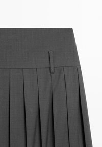 Section de jupe plissée gris foncé avec une large ceinture et une seule passants de ceinture sur un fond clair uni.