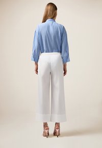 Blouse rayée bleu et blanc à manches longues, associée à un pantalon large blanc et des sandales à talons hauts roses.