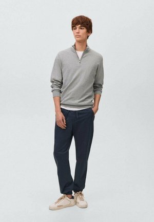 Gray zip-neck sweater, navy pants, and light sneakers on a model. Sweater features ribbed cuffs; pants have a relaxed fit. Simple design.