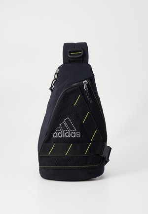 Sac banane noir Adidas avec poche avant en mesh, coutures diagonales vert néon, fermetures éclair, et boucle de sangle réglable.