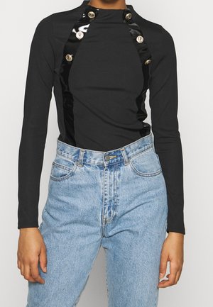 Sort langærmet top med satintrim og seks gyldne knapper, kombineret med lyseblå jeans med høj talje.