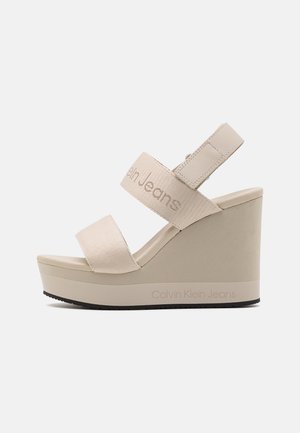 Sandalias de cuña beige con dos correas de tela, con el logo "Calvin Klein Jeans". Plataforma elevada con suela texturizada para mayor agarre.
