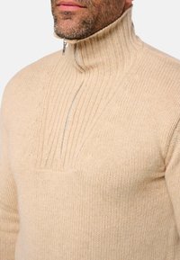 Beige Strickpullover mit hohem Kragen und halbzipper Design. Verfügt über eine gerippte Textur und subtile Details am Kragen und auf der Brust.