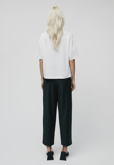 Bílý zkrácený tričko s krátkým rukávem v kombinaci s černými širokými kalhotami. Černé boty na blokovém podpatku doplňují celý outfit.