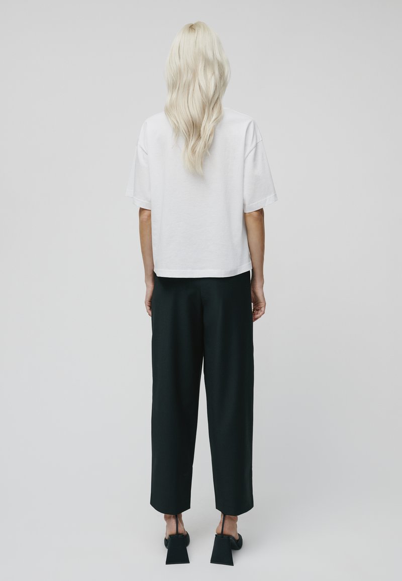 Weißes, kurzärmeliges, cropped T-Shirt in Kombination mit schwarzen, weiten Hosen. Schwarze, Blockabsatzschuhe runden das Outfit ab.