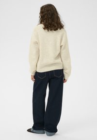 Krēmveida džemperis ar brīvu piegriezumu un ribotu apakšmalu, apvienots ar tumši ziliem platām biksēm ar piedurkņu apakšmalu un aizmugurējām kabatām.