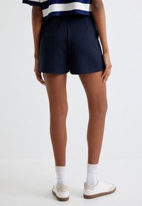 Shorts bleu marine en tissu doux, avec une coupe décontractée, des poches latérales et une taille élastique. Associés à des baskets blanches et des chaussettes mi-hautes.