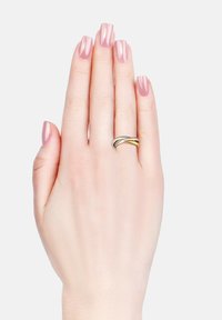 Anello intrecciato d'argento e oro su una mano con unghie rosa chiaro lucidate. La mano è rivolta con il palmo verso l'alto contro uno sfondo bianco semplice.