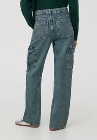 Wysokiej talii, luźne niebieskie dżinsowe spodnie cargo z dwoma dużymi bocznymi kieszeniami, toną szwów i wyblakłą strukturą.