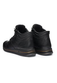 Stivaletti alla caviglia in pelle nera texturizzata con colletto imbottito, cerniere laterali e suole di gomma con una sottile striscia marrone, mostrati dalla parte posteriore.