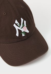 Cappello di cotone marrone con logo ricamato bianco, decorato con un fiore rosa e foglie verdi. Visiera curva e tessuto testurizzato.