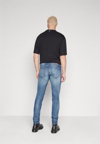 Jean en denim bleu avec une coupe slim, texture délavée et détails de couture. Associé à une chemise noire à manches courtes et des bottes noires.