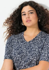 Top V-neck blu navy con motivo astratto bianco, maniche corte e una texture morbida. Adesivo al collo, vestibilità rilassata complessivamente.
