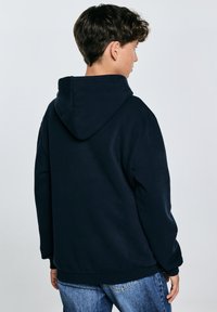 Sudadera azul marino fabricada en una suave mezcla de algodón, con capucha ajustable, puños y dobladillo acanalados. Combinada con jeans de color azul claro.