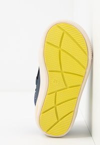 Podešev boty s texturovaným žlutým gumovým povrchem, který má cikcakovou strukturu a bílý okraj. Velikost označena jako 21.