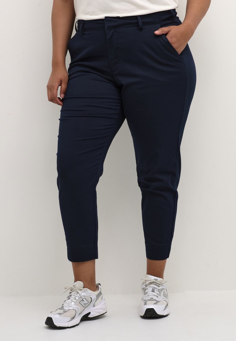 Navy blue tailored trousers in a stretchy fabric, featuring a flat front, side pockets, and a tapered design down to the ankle.