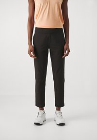 Black tailored pants with a smooth texture, cropped length, and an elastic waistband, paired with white athletic shoes and a peach top.