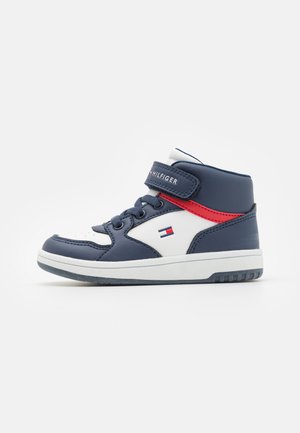 Zapatillas altas de color azul marino con detalles en blanco, cuero texturizado, correa ajustable y detalles en rojo. Incluye una suela plana y exhibición del logo.