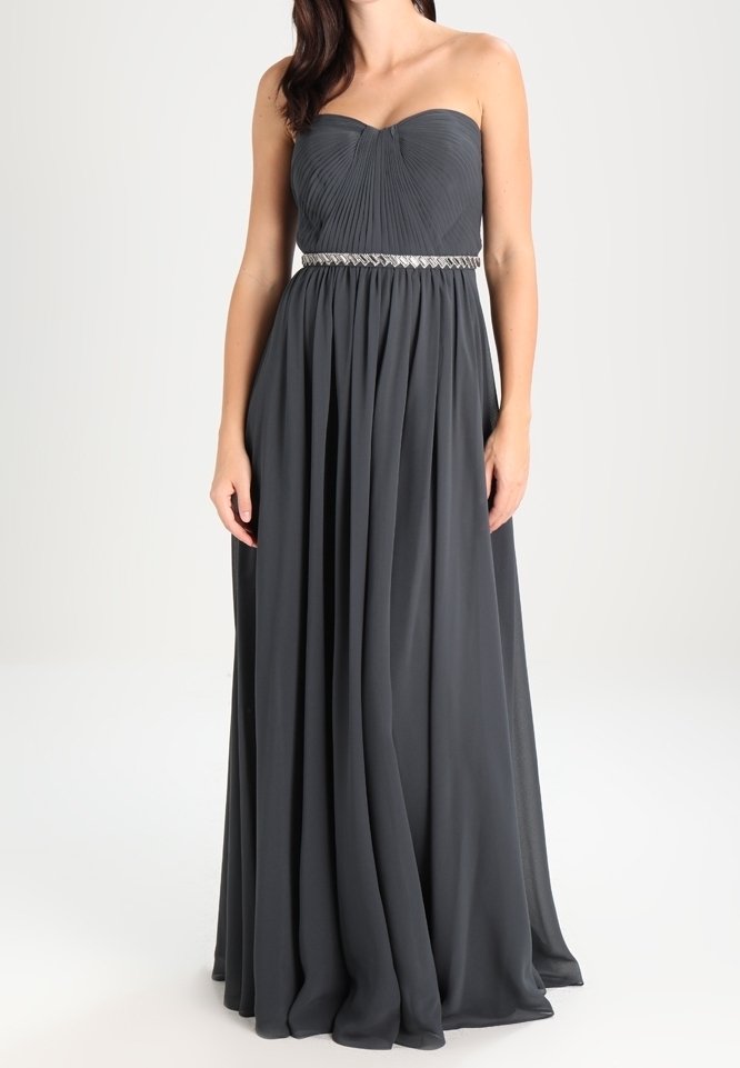 Robe longue grise foncée sans bretelles avec corsage plissé et ceinture argentée ornée de perles portée par une personne debout.