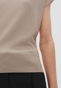 Top beige a maniche corte in morbido cotone liscio. Presenta un orlo ribattuto. Design semplice e strutturato con vestibilità rilassata.