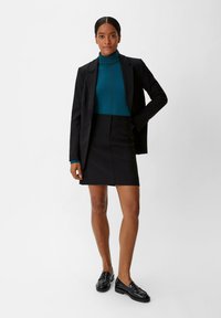 Schwarze maßgeschneiderte Blazer über einem türkisfarbenen Rollkragenpullover und einem schwarzen Minirock, kombiniert mit schwarzen Loafers. Glatte Texturen und eine figurbetonte Silhouette.