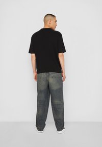 Must musta lühikeste varrukatega polo särk, mugav lõige, koos laia säärega pleekinud siniste teksadega, lõpetatud valgete jooksujalatsitega. Minimalistlik disain, nähtavad mustrid puuduvad.