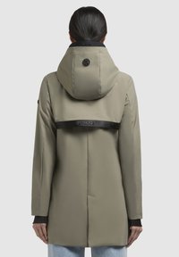 Giacca verde oliva chiaro con cappuccio e una cinghia nera sul retro. Tessuto liscio e maniche lunghe, design di lunghezza intermedia con dettagli minimi.