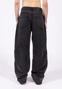 Luźne czarne spodnie dżinsowe z dużymi kieszeniami, metalowymi dodatkami i fakturowanym wykończeniem, charakteryzujące się wysokim stanem i elastycznymi ściągaczami przy kostkach.