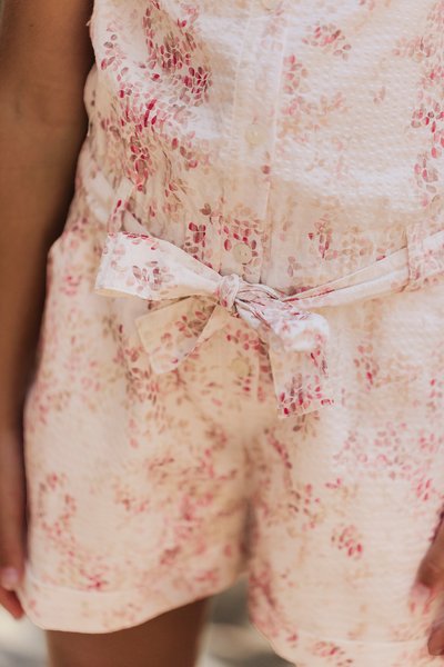 Vita tygshorts med ett blommönster i rosa och ljusbrunt. Har en knappstängning fram och ett tygbälte knutet i midjan.