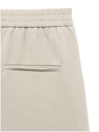 Nahaufnahme von beigefarbenen Stoffhosen mit elastischem Bund und einer einzelnen Paspeltasche auf der Rückseite.