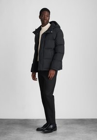 Black puffer jacket with a hood, quilted design, front snap closure, and side pockets. Worn over a light sweater and paired with black pants.