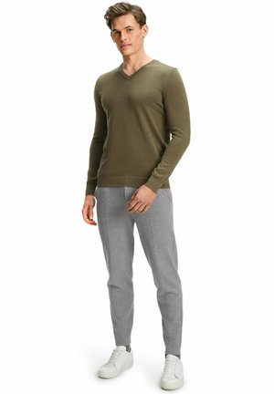 Pull en V vert olive associé à un jogging tapered gris clair. La tenue présente un design simple et est complétée par des baskets blanches.