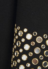 Svart textil med en uppsättning av guldaccentuerade, reflekterande cirkulära dekorationer i olika storlekar på ena sidan.