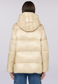 Giacca puffer beige chiaro con cappuccio foderato, forma boxy, motivo trapuntato e morbida lucentezza. Presenta maniche ampie e orlo cropped.