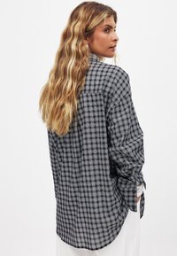 Checkered shirt with black and white patterns, long sleeves, relaxed fit, buttoned cuffs, slightly curved hem, made of lightweight fabric.