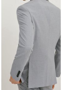 Helle graue Anzugjacke mit texturiertem Gewebe. Verfügt über einen einzelnen Schlitz, vier schwarze Knöpfe am Ärmel und strukturierte Schultern.