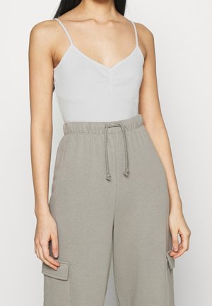 Light gray bodysuit with a v-neckline and ruching detail, paired with loose, gray sweatpants featuring an elastic waistband and side pockets.