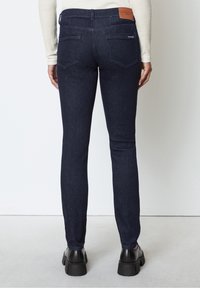 Tmavě modré džínové kalhoty slim fit s kapsami na zadní straně a koženou nášivkou na pase. Hladká textura a minimální detaily.