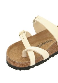 Sandal di un beige chiaro con cinghie incrociate, soletta in sughero e suola in gomma nera testurizzata. Caratterizzato da un dettaglio in metallo sulla fibbia delle cinghie.