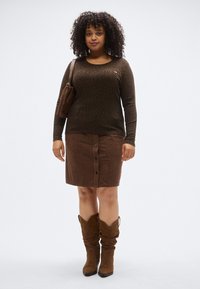 Rudas ilgomis rankovėmis megztinis su leopardų raštu, derinamas su ruda kordurojaus sijonu su priekinėmis sagomis; rudi laisvo stiliaus ilgi batai iki kelių.