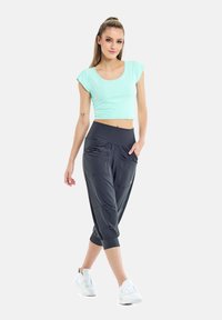 Top corto de menta, pantalones joggers negros ajustados con bolsillos y zapatillas blancas. Los joggers tienen una cinturilla ancha y un tejido suave y texturizado.