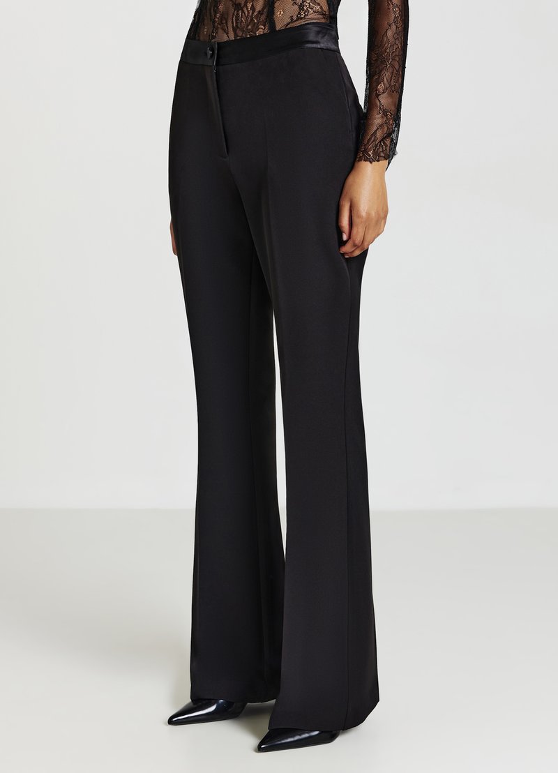 Schwarze maßgeschneiderte Hosen mit einem ausgestellten Bein Design, hergestellt aus glattem Stoff. Sie verfügen über einen flachen Bund und einen dezenten Verschluss vorne.