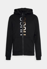 Felpa nera con cerniera frontale, tasca anteriore, cappuccio con coulisse e design testuale riflettente in argento e oro. Polsini e bordo a costine.