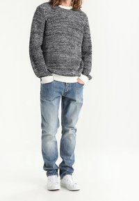 Maglione grigio a maglia con polsini bianchi, abbinato a jeans azzurri chiari e sneaker bianche. Il maglione presenta un motivo testurizzato su tutta la superficie.