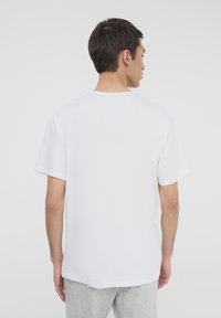 T-shirt bianco in cotone con maniche corte, scollatura a girocollo e vestibilità rilassata, mostrato da dietro su uno sfondo chiaro uniforme.